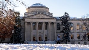 A student walks in front of Wilson Library in the snow.