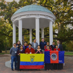 A group of students pose in front of the old well holding an Ecuadorian flag and a UNACH flag.