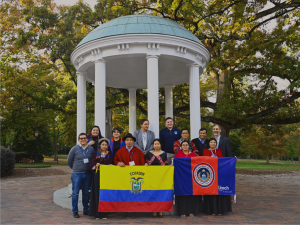 A group of students pose in front of the old well holding an Ecuadorian flag and a UNACH flag.