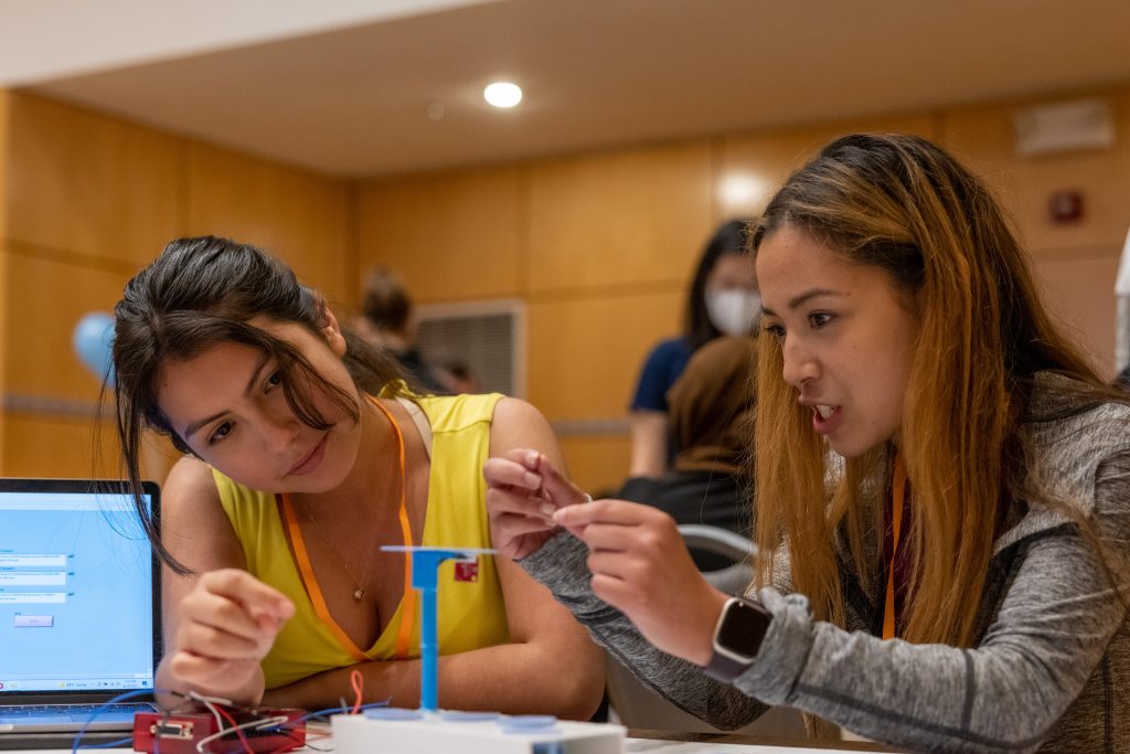 Two female students work together at a table solving an engineering problem.