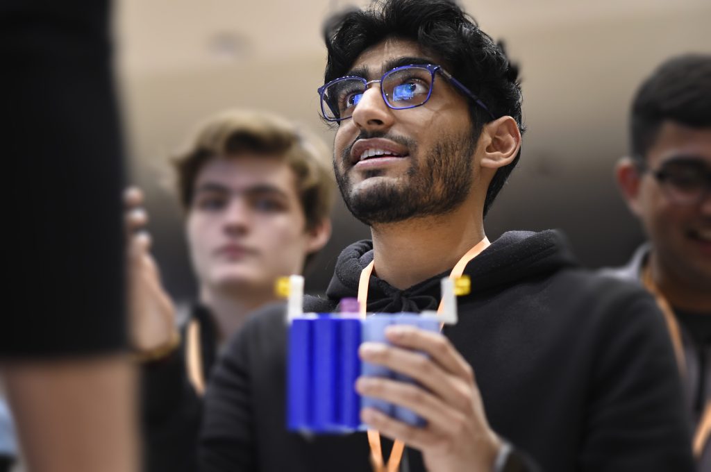 A student holds a small, 3D-printed object and chats about it with curious onlookers.