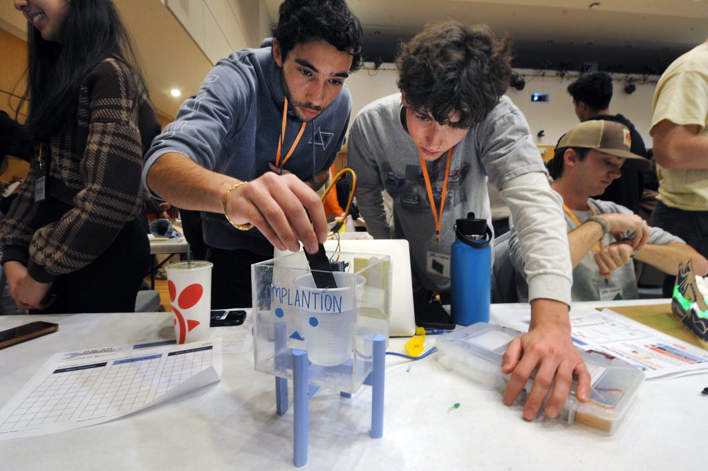 Two students lean into a project at MakerFest to conduct an experiment.