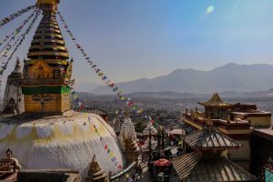 An-aerial-drone-photo-of-Swayambhu-shows-the-main-stupa-and-temple-complex-in-the-foreground-and-Kathmandu-in-the-background.