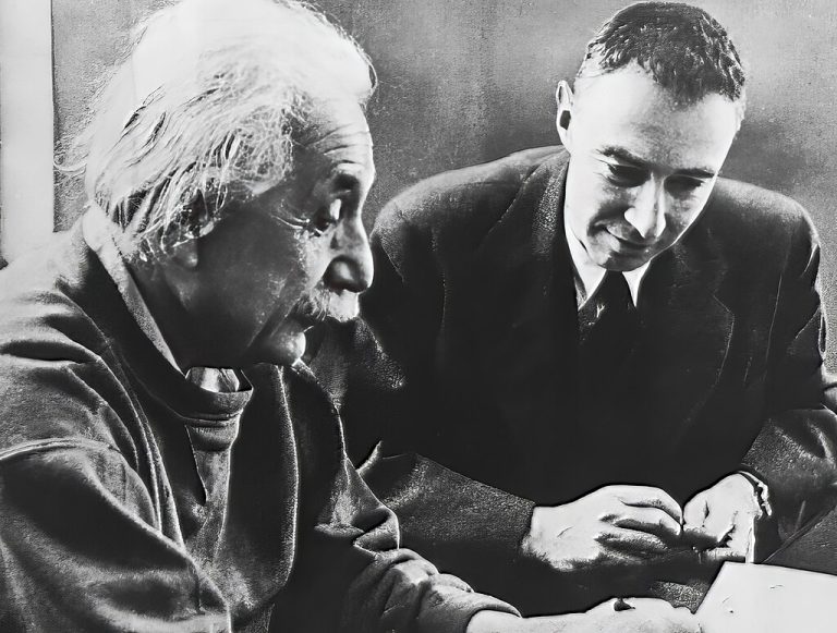 Archive photo of Albert Einstein and Robert Oppenheimer sitting and looking over a notebook together.