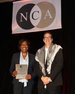 Patricia Parker (left) holds up her award next to another scholar, in front of a banner that reads "NCA."