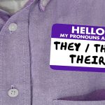 Closeup of a person wearing a purple shirt with a name badge that says "Hello: They/Them/Their" on it.