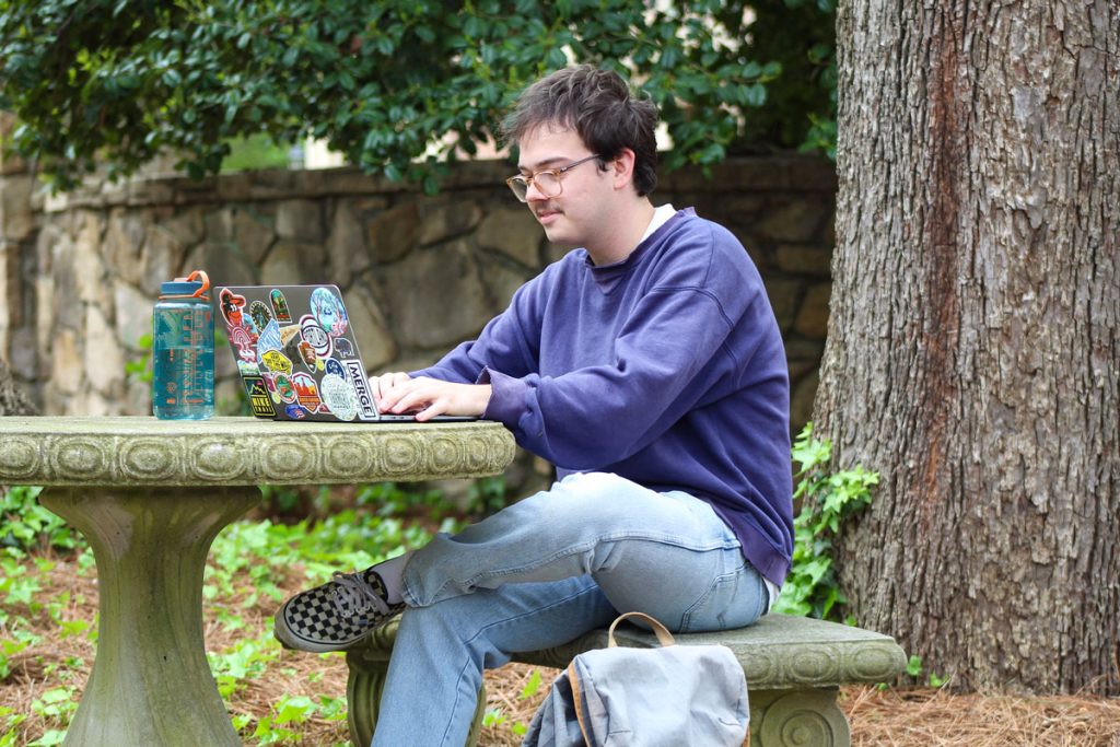Calvin Mueller sits at a circular stone table, working on his laptop.