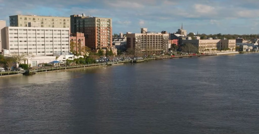 Overhead view of the Cape Fear River in Wilmington with buildings lining the waterfront.