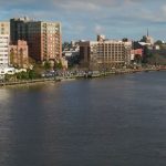 Overhead view of the Cape Fear River in Wilmington with buildings lining the waterfront.