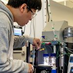 Hyuenwoo Yang in the lab, tweaking controls on a machine with wires hooked to two vials of liquid.
