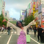 A horizontal image of Xenia Weakly, arms outstretched to the sky, standing on a street in Akihabara, Japan.