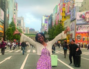 A horizontal image of Xenia Weakly, arms outstretched to the sky, standing on a street in Akihabara, Japan.