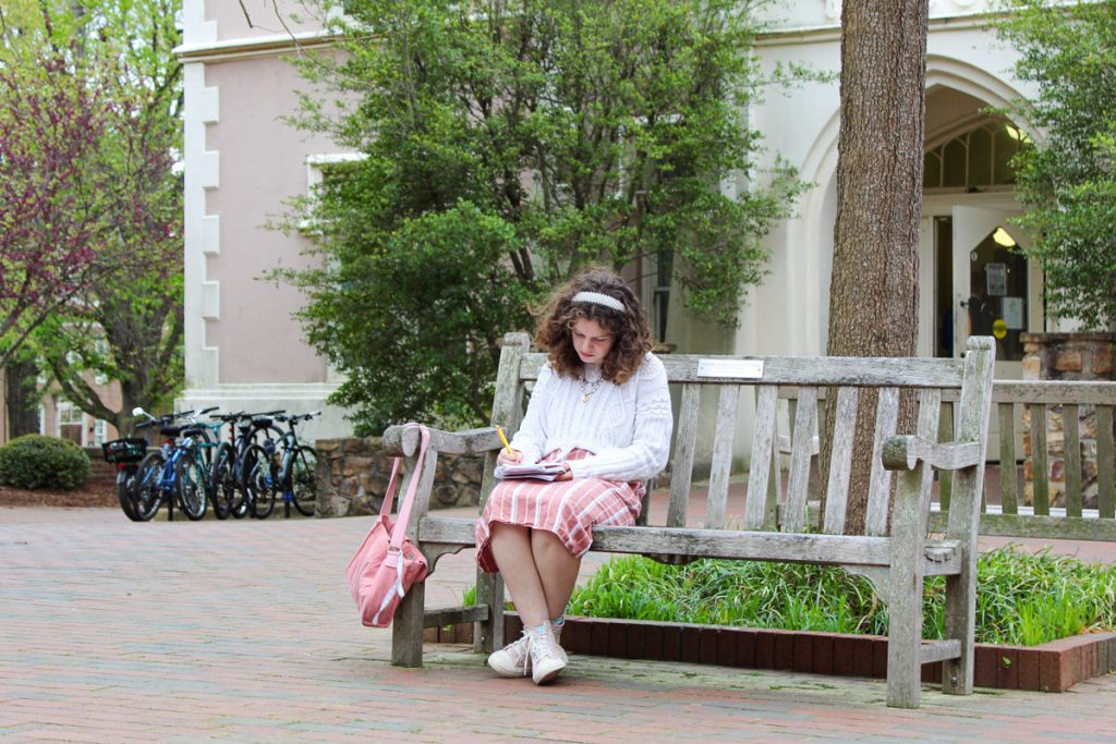 Maggie Dunn writes in a notebook as she sits on a bench outside the Campus Y.