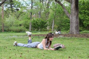 Naomi Ovrutsky lays on her stomach reading a book inside the open green space of Coker Arboretum.