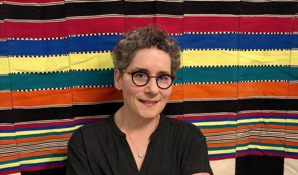 Victoria Rovine stands in front of a colorful background featuring African textiles.