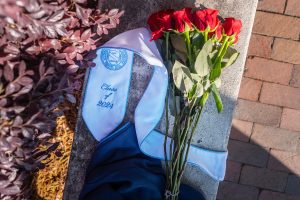 A 2024 graduation sash sits on the ground with a bouquet of flowers on top of it.