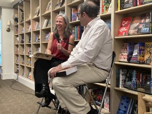 Kathleen DuVal and Keith Richotte Jr. sit and chat in front of a bookshelf full of books.