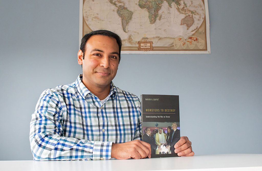 Navin Bapat holds a copy of his book and smiles at the camera.