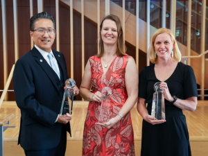 Three faculty members hold awards and stand in a row, smiling at the camera.