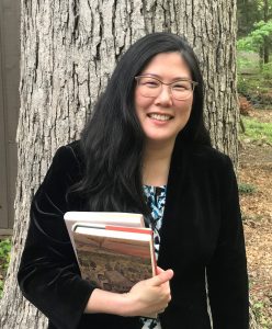 Headshot of Heidi Kim in front of a tree holding books.